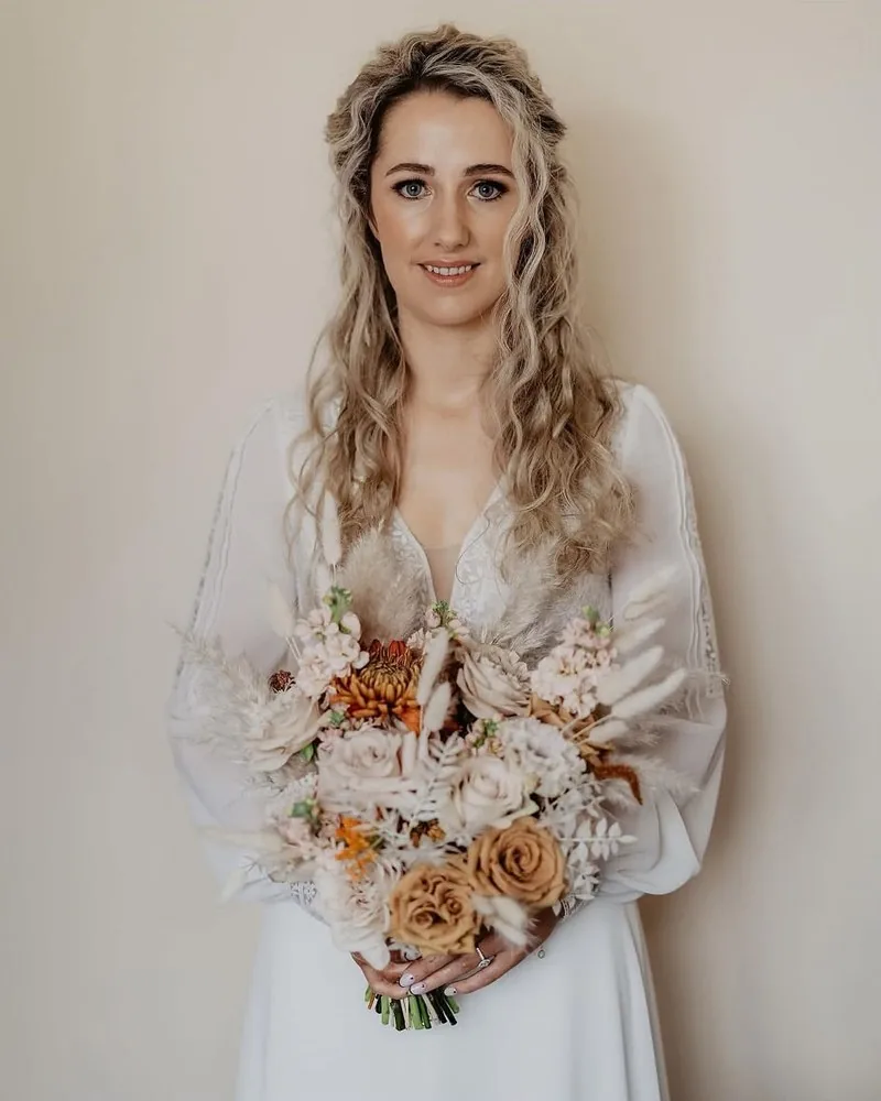 Bride Kerri with natural textured waves pinned back from her face, holding a dried-flower bouquet